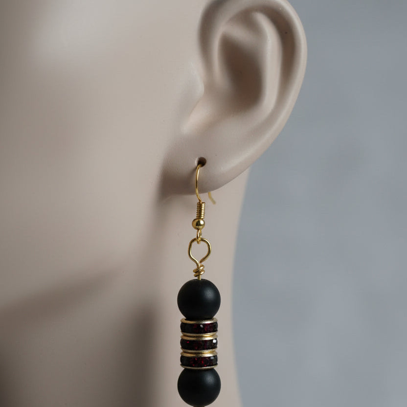 Pair of black beaded earrings with gold accents on a gray surface