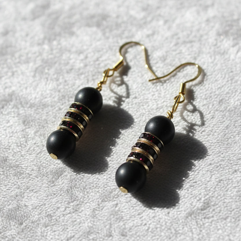 Pair of black beaded earrings with gold accents on a gray surface