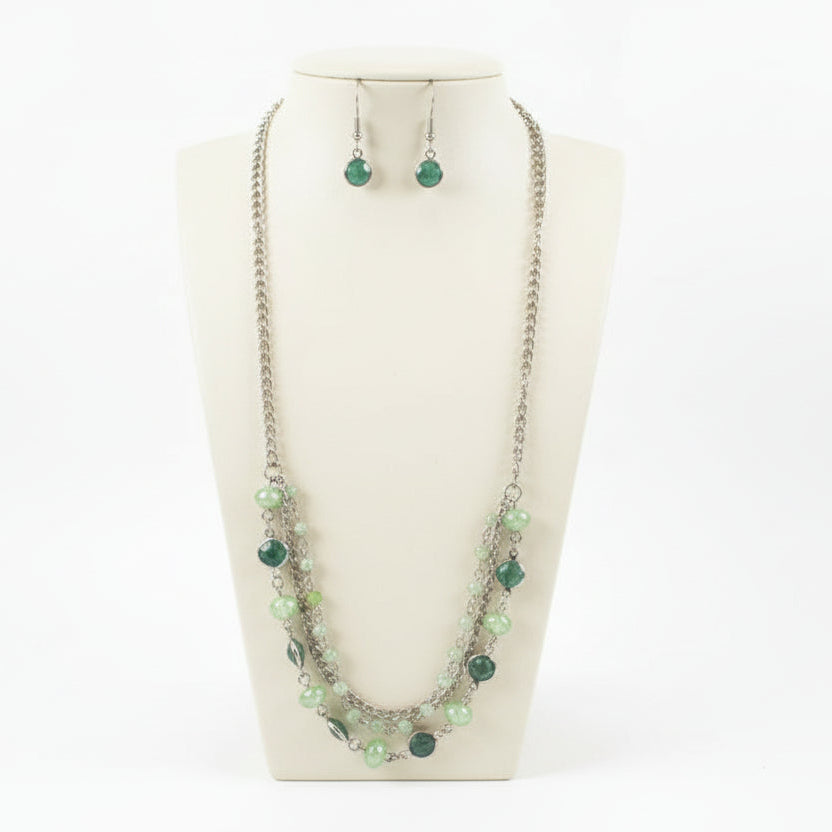 Necklace with green beads and matching earrings on a black stand.
