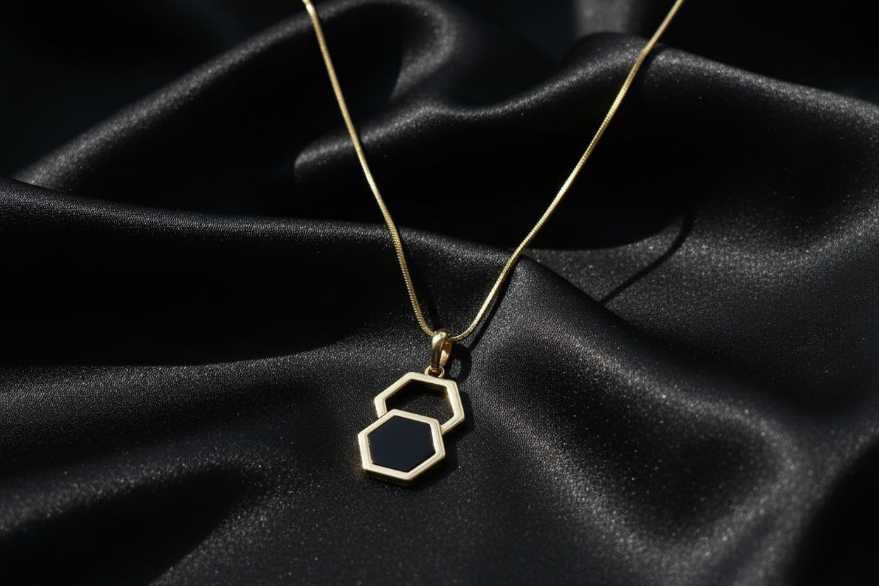 Gold necklace with a hexagonal pendant on a textured gray surface