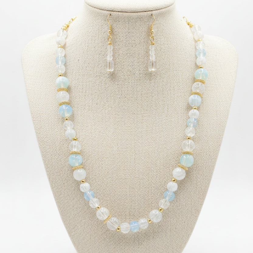 A beaded necklace and matching drop earrings displayed on a black jewelry bust. The jewelry features white and light blue marbled beads with small gold spacer rings and gold-tone hooks.