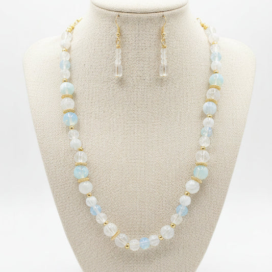 A beaded necklace and matching drop earrings displayed on a black jewelry bust. The jewelry features white and light blue marbled beads with small gold spacer rings and gold-tone hooks.