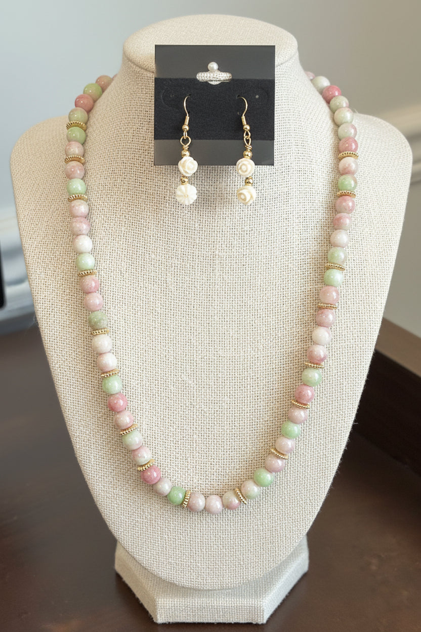 A pastel beaded necklace and matching drop earrings displayed on a black jewelry bust. The beads are pink, mint green, and white with small gold spacer rings and gold-tone hooks.